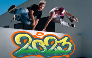 Two athletes jumping over wall with 2023 graffiti.